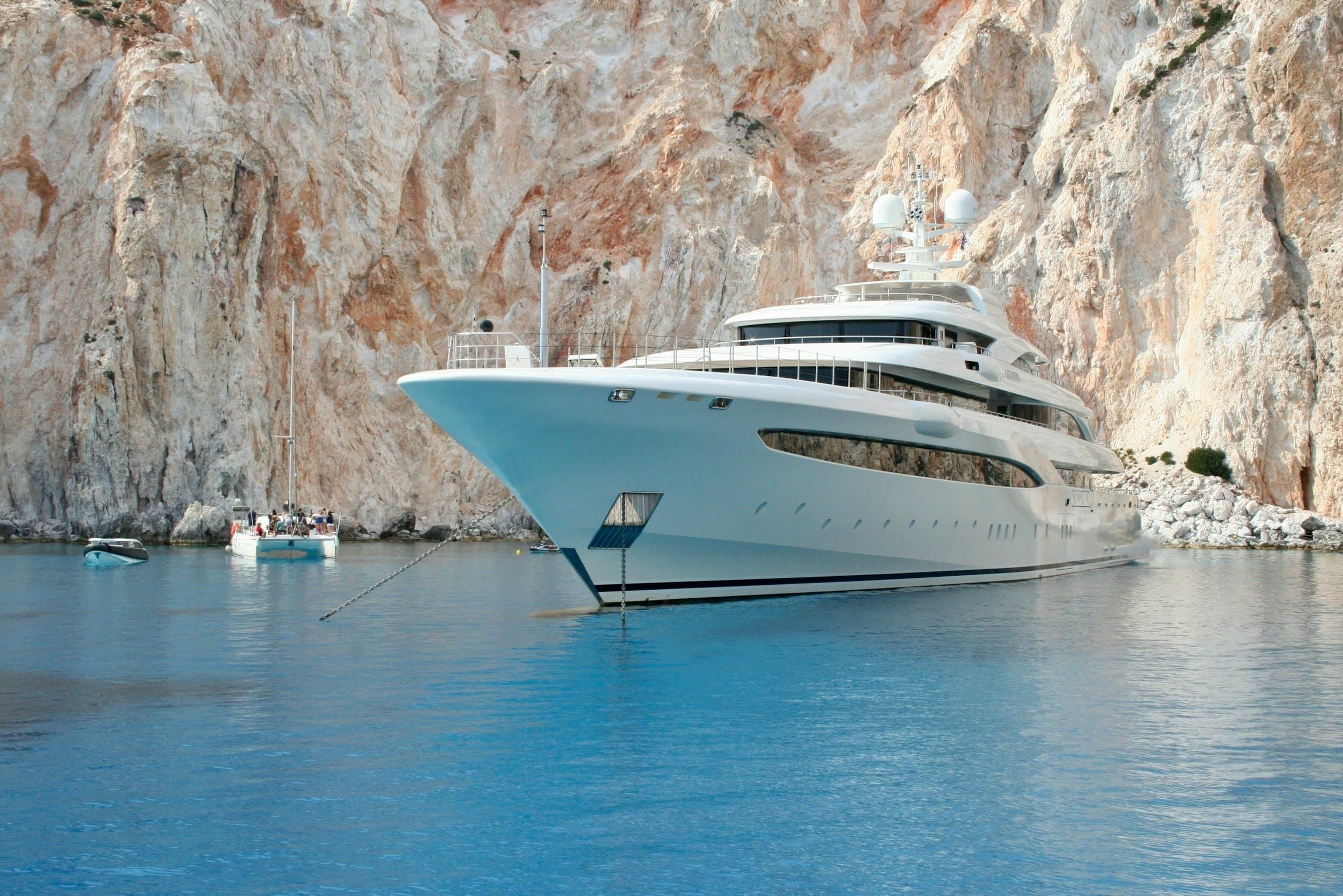 A crewed motor yacht at anchor in a Mediterranean bay at golden hour, tender alongside