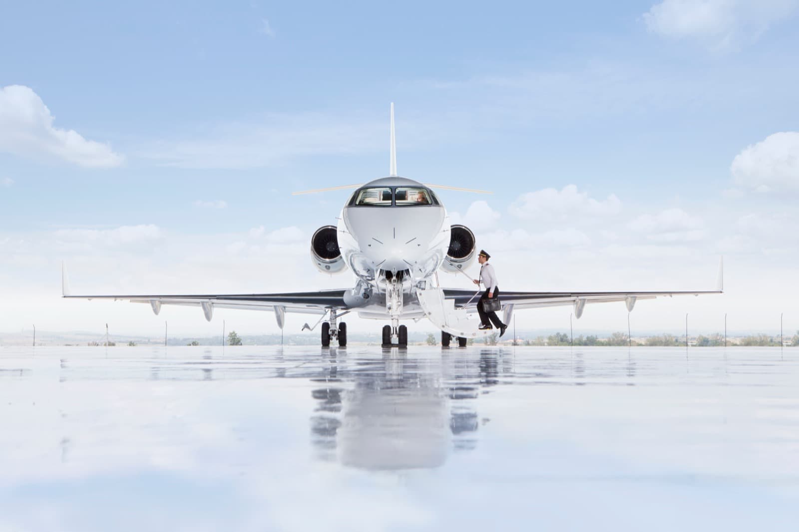 A heavy private jet on the ramp at a London business aviation airport in summer light, ground crew positioning bags